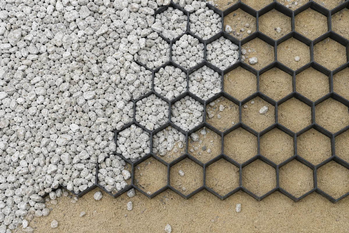 Stabilisateur alvéolaire noir posé sur un lit de sable avant remplissage de gravier gris, vue de dessus